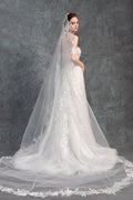 Woman wearing a white wedding dress with a long veil against a gray background