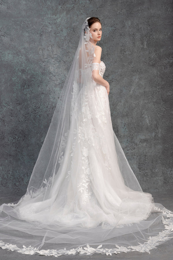 Woman wearing a white wedding dress with a long veil against a gray background